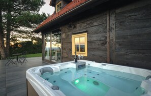 Eine Holzhütte mit einem Whirlpool auf einer Terrasse, einer Glastür, die zu einer Veranda führt, und einem Fenster mit gelbem Rahmen.