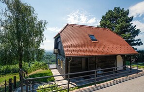 Ein zweistöckiges Steinhaus mit rotem Ziegeldach, einem Balkon und Blick auf eine üppige Landschaft.