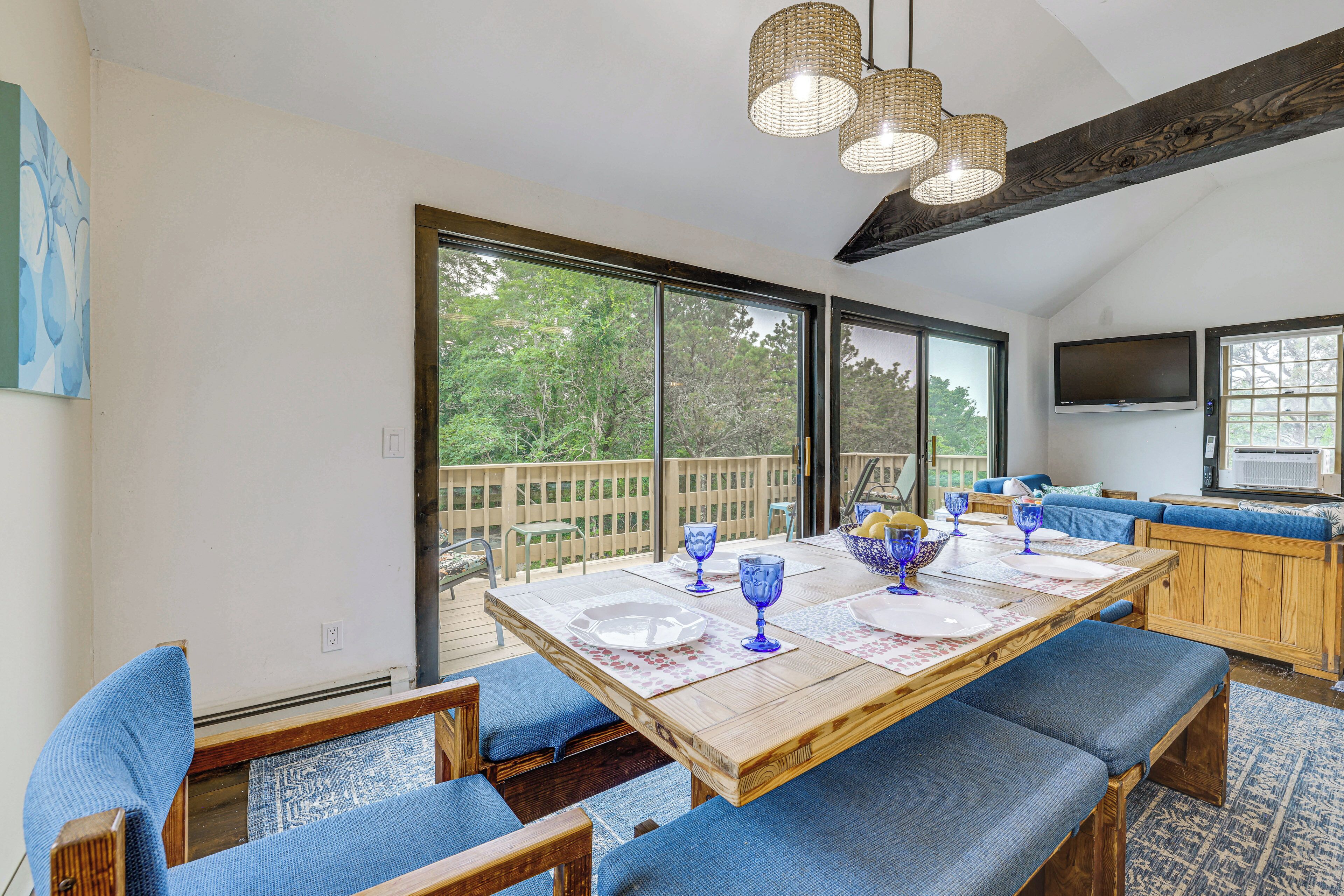 Un comedor amplio con una mesa grande dispuesta para seis personas, bancos de madera y vistas al exterior a través de amplios ventanales corredizos.