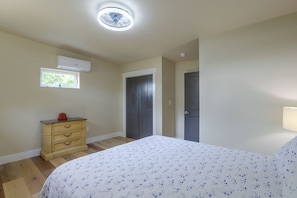 A bedroom with a bed, a dresser, a window, and an air conditioning unit. - Blue Heron - New Modern Home in Carrabelle (Carrabelle)
