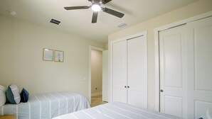 Un dormitorio con dos camas, un ventilador de techo y una puerta que da a otra habitación.