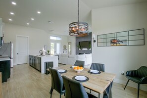 A modern kitchen with a dining area, featuring a wooden table, black chairs, and a central island with a sink. - Poolside Paradise in Northwest Cape Coral! (Cape Coral)