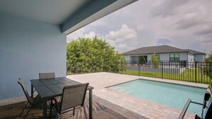 Zona de piscina con mesa y sillas, patio cercado y un edificio al fondo.