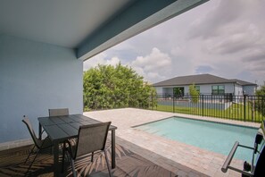 Ein Poolbereich mit Tisch und Stühlen, ein umzäunter Garten und ein Gebäude im Hintergrund.