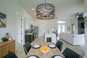 Une cuisine moderne avec des meubles blancs, un îlot central et un coin repas comprenant une table en bois et des chaises noires.