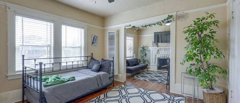 A bedroom with a bed, a ceiling fan, a window, a plant, and a fireplace.