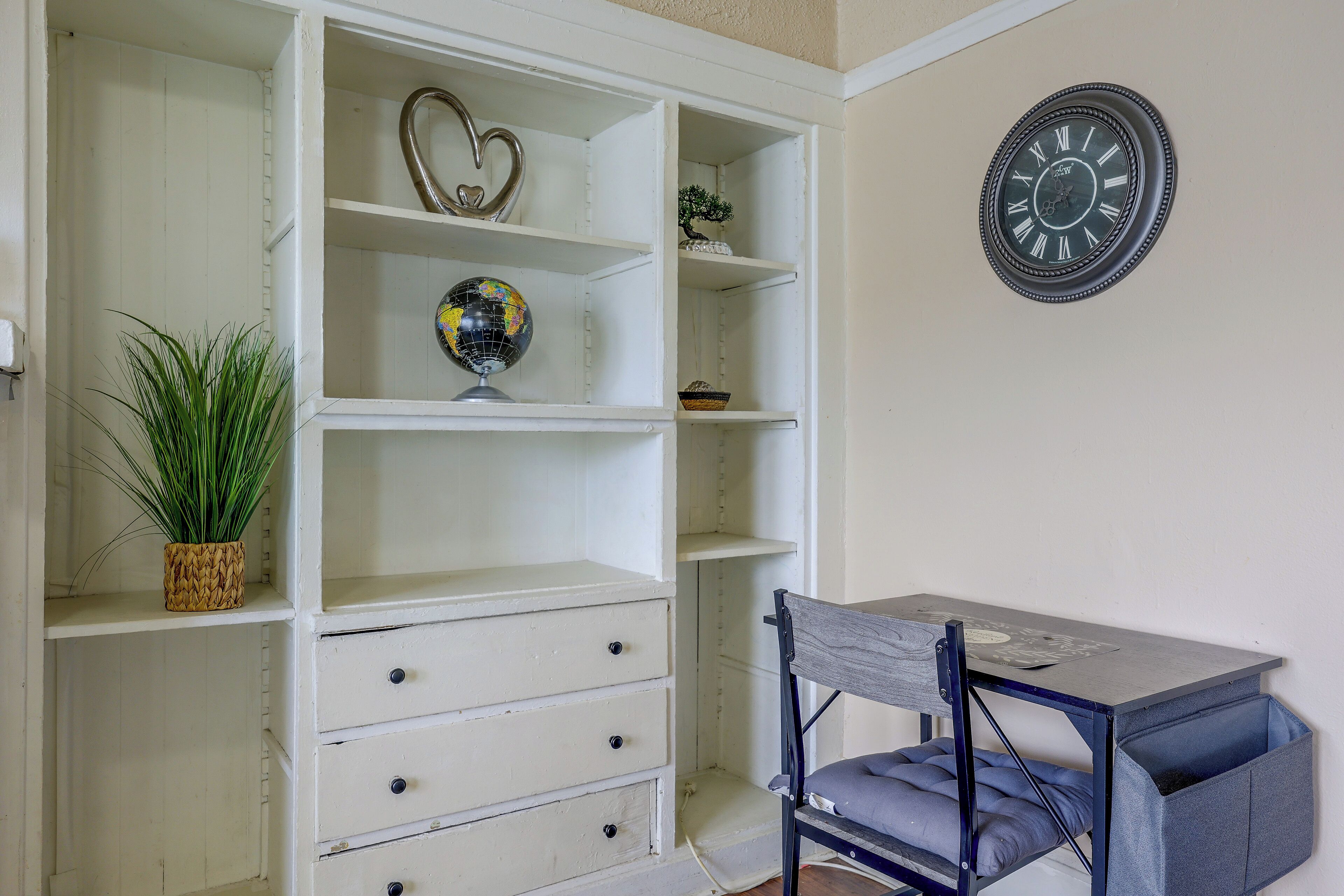 A room with a desk, drawers, a globe, a heart-shaped ornament, and a clock on the wall.