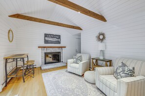 A room with a fireplace, a wooden ceiling, a white wall with a fish illustration, a round mirror, a striped sofa, and a small table. - Minutes Away From the Best Beaches in Cape Cod! (South Dennis)