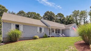 A single-story house with a covered porch, a garage, and a well-maintained lawn. - Minutes Away From the Best Beaches in Cape Cod! (South Dennis)