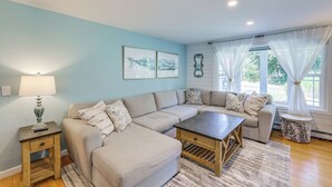 A living room with a sectional sofa, a coffee table, a lamp, and artwork on the wall. - Minutes Away From the Best Beaches in Cape Cod! (South Dennis)