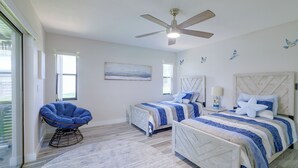 Quarto com duas camas, ventilador de teto, cadeira de balanço e vista para o exterior.
