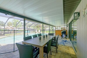 Ein überdachter Patio-Bereich mit Tisch und Stühlen, ein Pool im Hintergrund und Blick auf die umliegende Nachbarschaft.