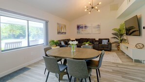 Uma sala de estar moderna com uma mesa de jantar redonda, sofás cinzas estofados e uma janela grande que oferece vista para o exterior.