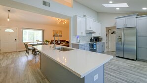 Uma cozinha moderna com ilha central, eletrodomésticos de aço inoxidável e área de jantar com vista para a sala de estar.