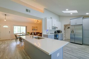 Eine moderne Küche mit Kochinsel, Edelstahlgeräten und einem Essbereich mit Blick zum Wohnzimmer.
