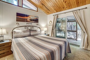 A bedroom with a large bed, wooden headboard, two bedside tables with lamps, a window with curtains, and a wall-mounted artwork. - Walk to Beach! Home w/ Sunroom in Anchor Bay (Gualala)