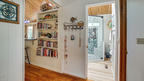 A room with wooden flooring, a bookshelf filled with books, a decorative fish sculpture, and a wall-mounted sign. - Walk to Beach! Home w/ Sunroom in Anchor Bay (Gualala)