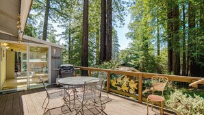 An outdoor deck with a table and chairs, surrounded by tall trees. - Walk to Beach! Home w/ Sunroom in Anchor Bay (Gualala)