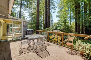 Eine Terrasse im Freien mit Tisch und Stühlen, umgeben von hohen Bäumen.