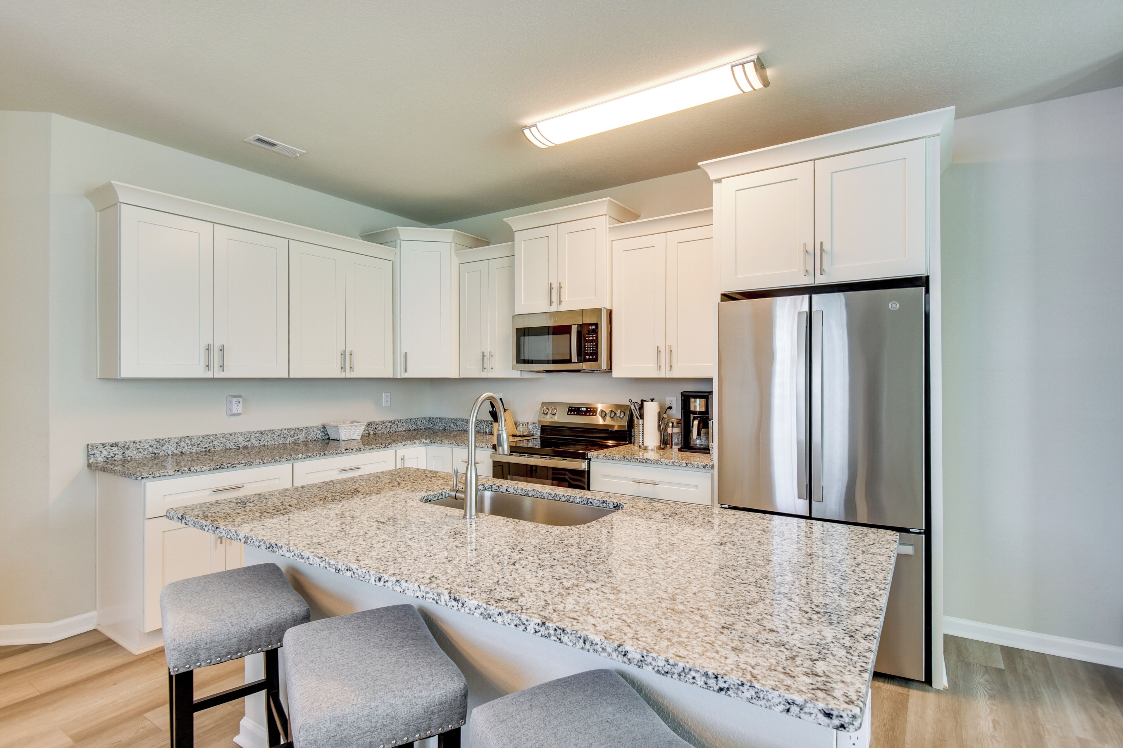 A modern kitchen with white cabinets, a stainless steel refrigerator, a built-in oven, and a granite countertop.