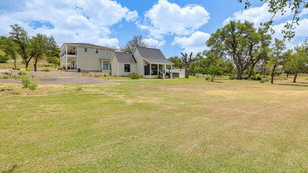 A two-story house with a covered porch, a fenced yard, and mature trees. - Hot Tub & Fire Pit! Texas Wine Country Retreat (Fredericksburg)