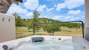 A hot tub with a view of a grassy landscape and trees. - Hot Tub & Fire Pit! Texas Wine Country Retreat (Fredericksburg)
