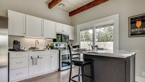 A modern kitchen with white cabinetry, a built-in microwave, and a large island with bar stools. - Hot Tub & Fire Pit! Texas Wine Country Retreat (Fredericksburg)