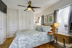 A bedroom with a bed, a desk with a lamp, a ceiling fan, and a window with curtains. - Free Parking! Waikiki Condo, 3BR, 5BDs, Sleeps 6! (Honolulu)
