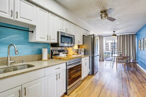 A modern kitchen with white cabinets, stainless steel appliances, a wooden countertop, and a dining area with a table and chairs. - Waikiki Penthouse, 1 Parking, 3BR, 5BDs, Sleeps 6 (Honolulu)
