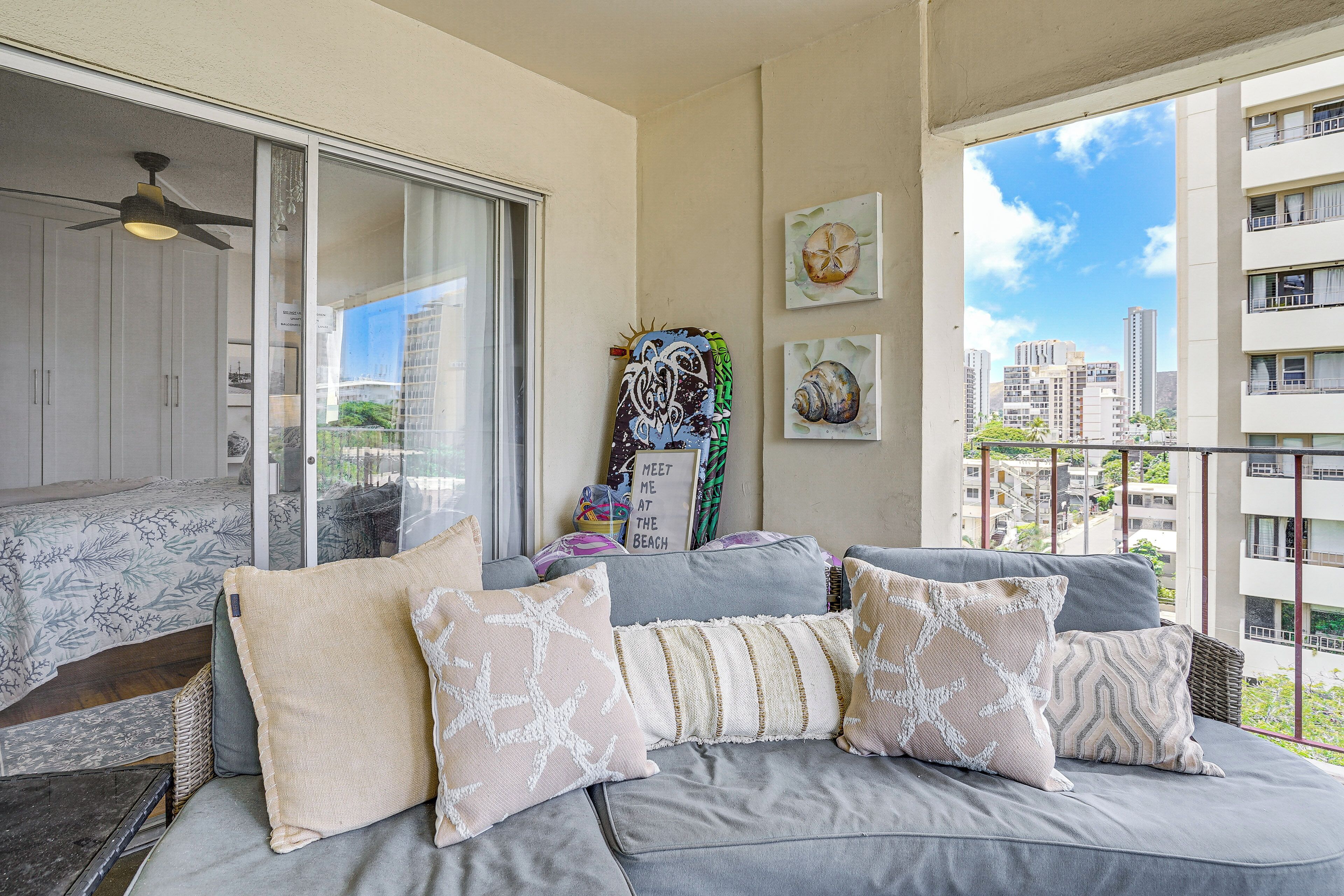A balcony with a grey sofa, cushions, and a view of the cityscape.
