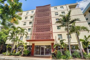 A multi-story hotel with a central entrance, surrounded by palm trees and a variety of plants. - Free Parking! Waikiki Condo, 3BR, 5BDs, Sleeps 6! (Honolulu)