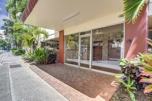 A building entrance with a glass door, a tiled walkway, and surrounding greenery. - Free Parking! Waikiki Condo, 3BR, 5BDs, Sleeps 6! (Honolulu)