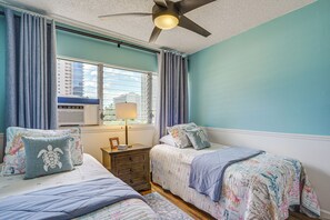 A bedroom with two beds, a ceiling fan, a window with curtains, and a nightstand with a lamp. - Waikiki Penthouse, 1 Parking, 3BR, 5BDs, Sleeps 6 (Honolulu)