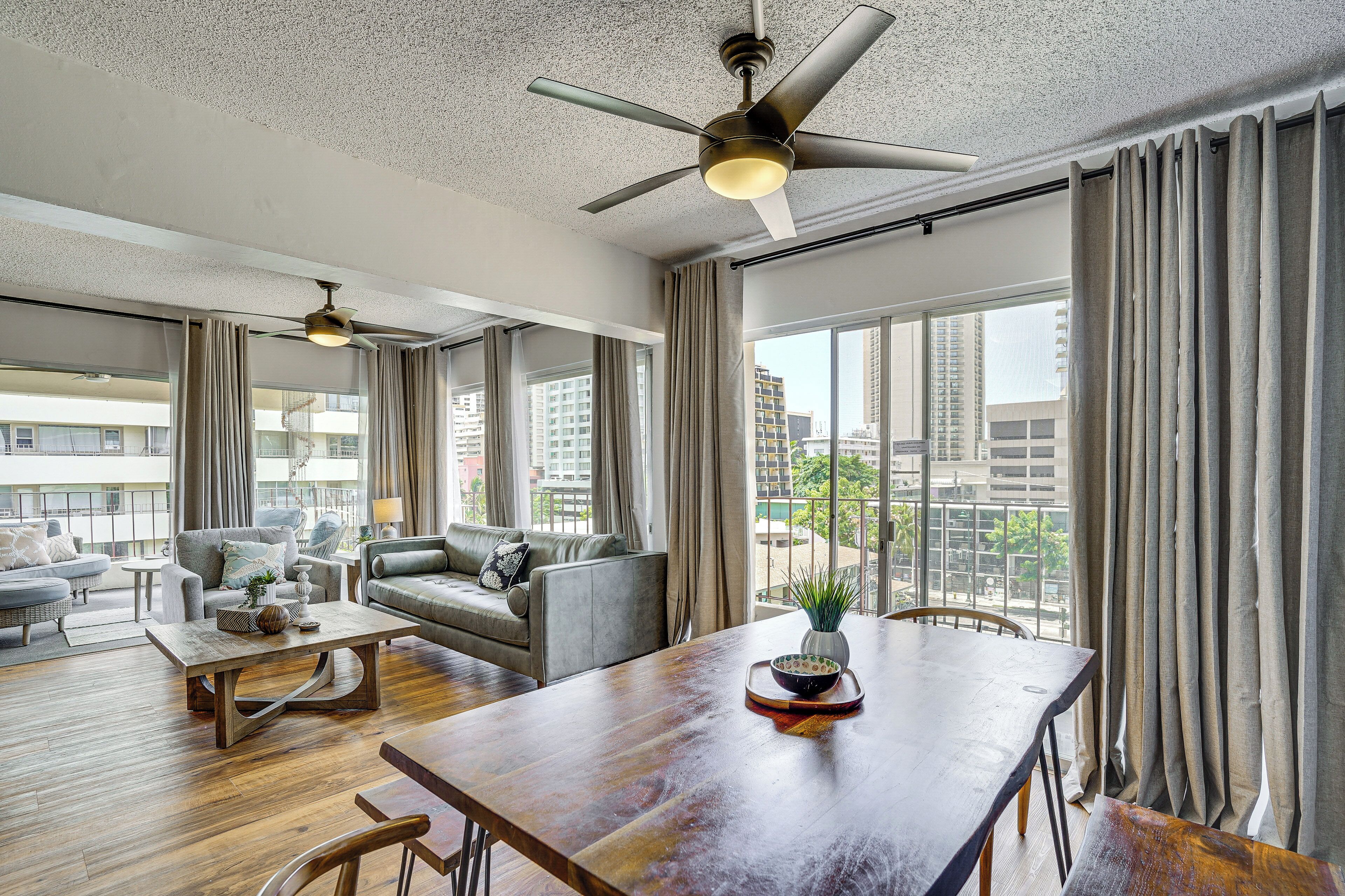 Un vaste salon doté d’un haut plafond, d’un ventilateur de plafond, d’une table à manger et offrant une vue sur la ville grâce à de grandes fenêtres.
