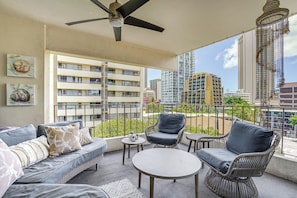 A balcony with a ceiling fan, wicker furniture, and a view of high-rise buildings. - Waikiki Penthouse, 1 Parking, 3BR, 5BDs, Sleeps 6 (Honolulu)