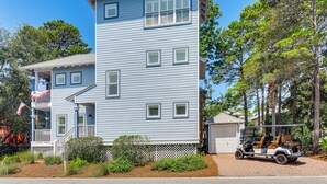 A two-story residential building with a garage, a covered porch, and a golf cart parked in front. - Walkable 30A Beach House: 2 Community Pools, Bikes (Santa Rosa Beach)