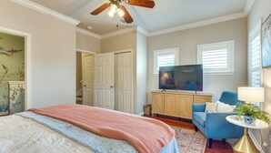 A bedroom with a bed, a television, a blue chair, a lamp, and a ceiling fan. - Walkable 30A Beach House: 2 Community Pools, Bikes (Santa Rosa Beach)