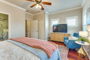 Ein Schlafzimmer mit einem Bett, einem Fernseher, einem blauen Sessel, einer Lampe und einem Deckenventilator.