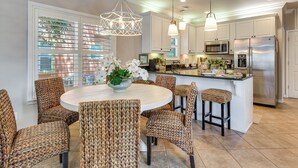 A modern kitchen with a central island, stainless steel appliances, and wicker chairs around a round table. - Walkable 30A Beach House: 2 Community Pools, Bikes (Santa Rosa Beach)