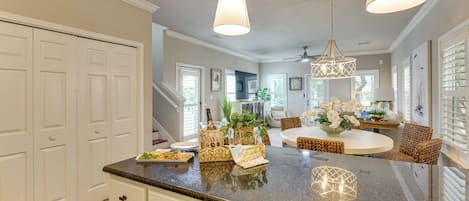 Una cocina con isla central, muebles blancos y un comedor con sillas de mimbre.