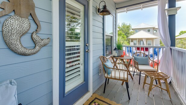 A porch with wicker furniture, a decorative wall piece, and a view of a neighboring house. - Walkable 30A Beach House: 2 Community Pools, Bikes (Santa Rosa Beach)
