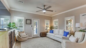 A spacious living room with a ceiling fan, a large window with blinds, a white sofa, a beige armchair, and a patterned rug. - Walkable 30A Beach House: 2 Community Pools, Bikes (Santa Rosa Beach)