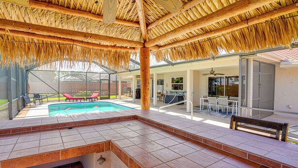 Uma área de piscina com cobertura de palha, uma banheira de hidromassagem e um espaço de estar coberto ao ar livre.