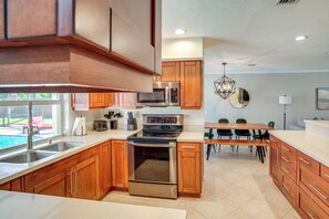 A modern kitchen with wooden cabinets, stainless steel appliances, and a dining area with a table and chairs. - Quiet Home 1 Mi to Savannas Preserve State Park! (Port St. Lucie)