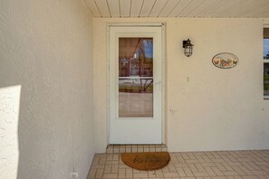 A white door with a glass panel, a doormat with 'hello' inscribed, a wall-mounted light fixture, and a circular sign with a bicycle and flowers. - Quiet Home 1 Mi to Savannas Preserve State Park! (Port St. Lucie)