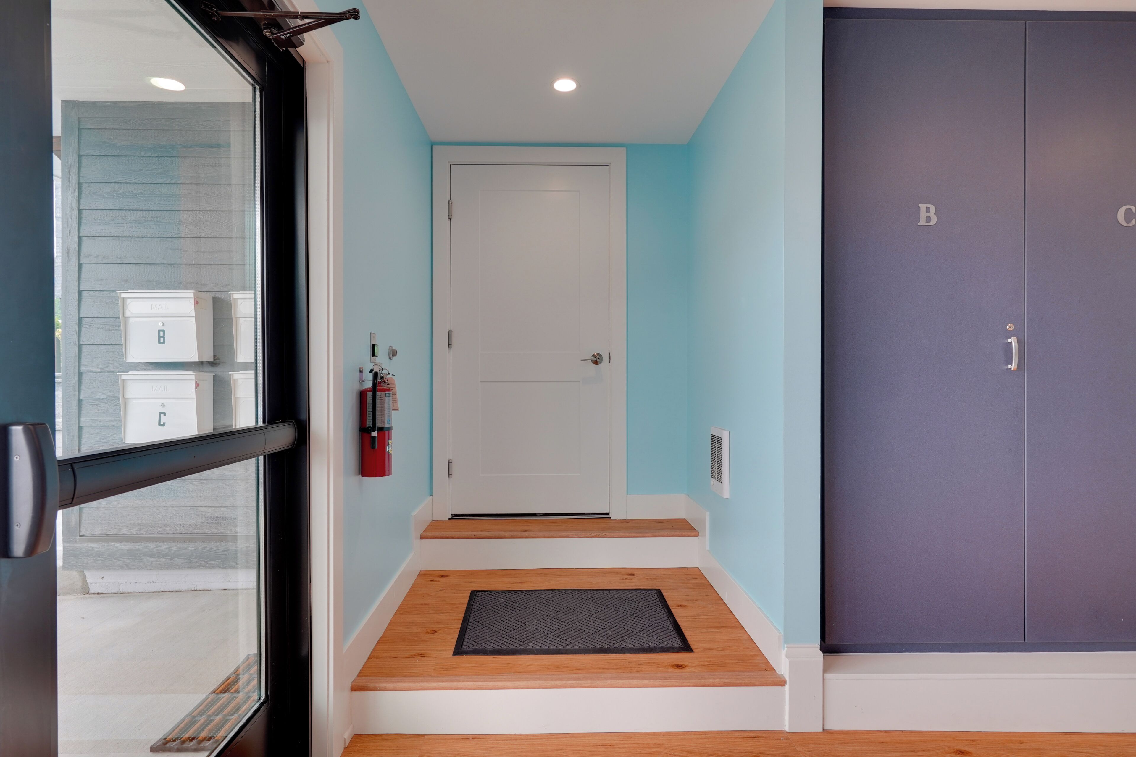 A hallway with a white door, a mailbox, and a fire extinguisher.