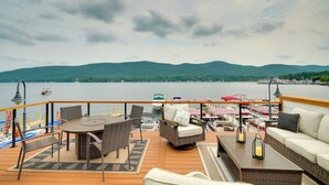 A deck with outdoor furniture, a view of a lake, and mountains in the distance. - Brand-New Luxury Lakefront Condo - 2200 Sq Ft! (Lake George)