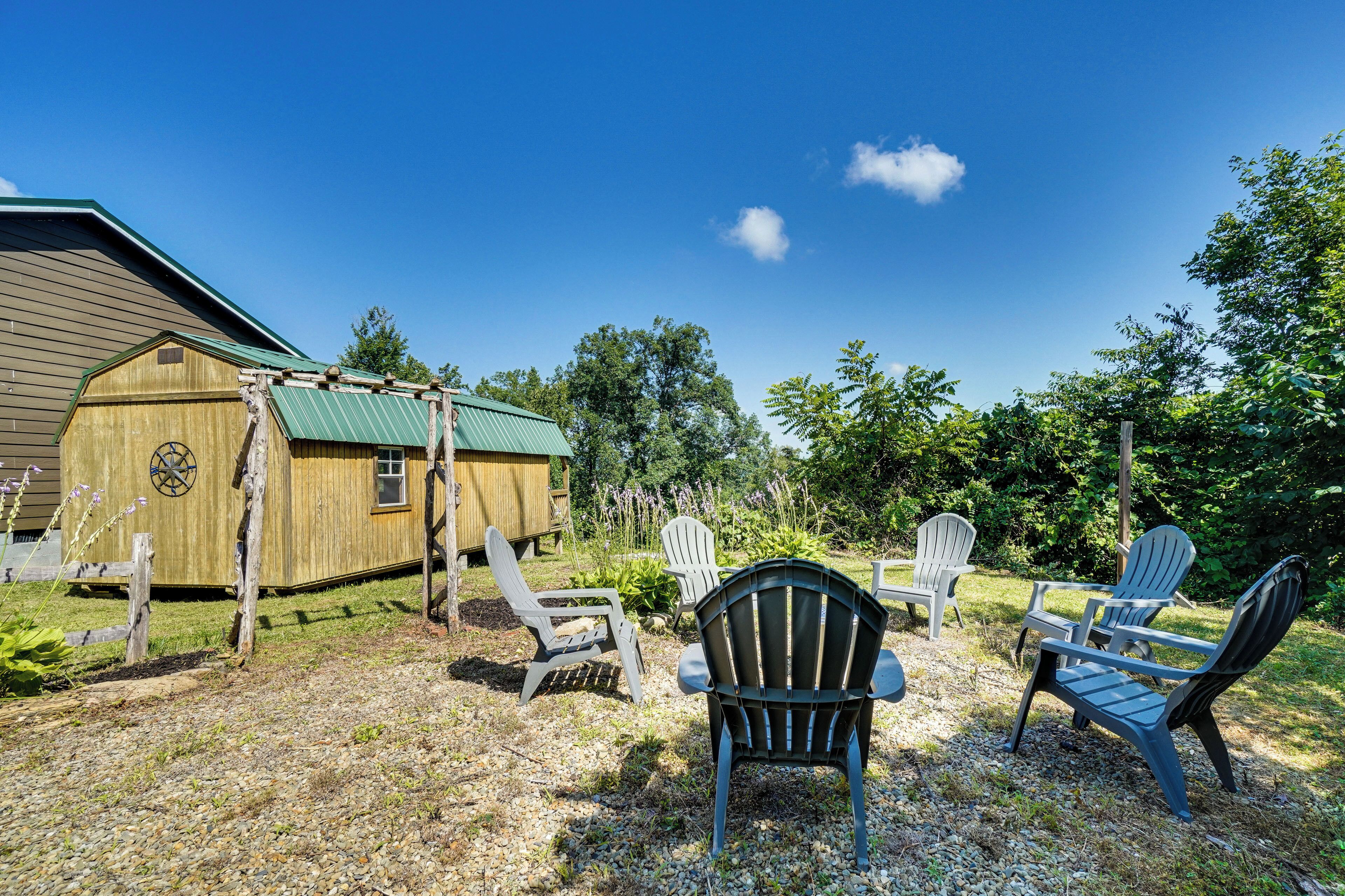 A wooden structure with a green roof, surrounded by gravel and greenery, with Adirondack chairs arranged for seating.