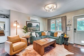 Ein Wohnzimmer mit Ledersessel, grünem Sofa, Couchtisch aus Holz und einem Gemälde an der Wand.