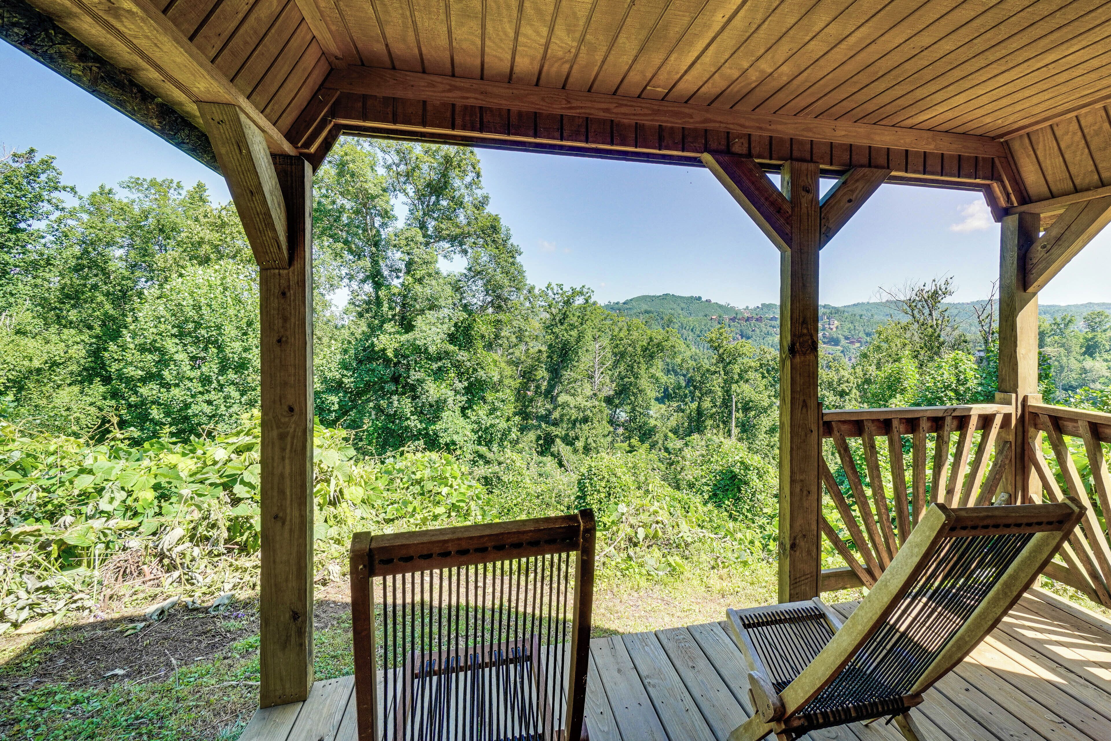 A wooden deck with two chairs and a table, overlooking a forested landscape.
